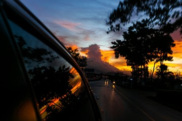 Fototapeta na wymiar Reflection Of Silhouette Trees And Orange Sky On Car Window