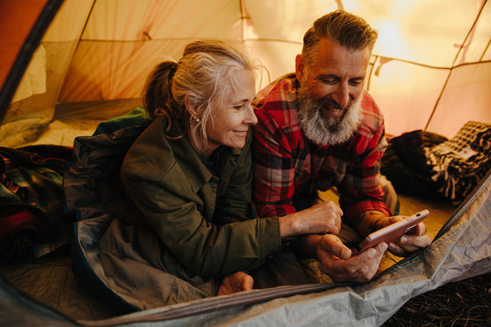 Happy senior couple using phone inside tent on camping trip