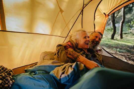 Senior couple laughing and cuddling inside tent in bedroll