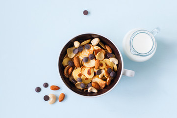 Tiny pancake cereal in a bowl with nuts, chocolate and milk.