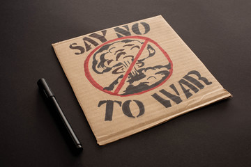 marker near cardboard placard with say no to war lettering and explosion in stop sign on black background