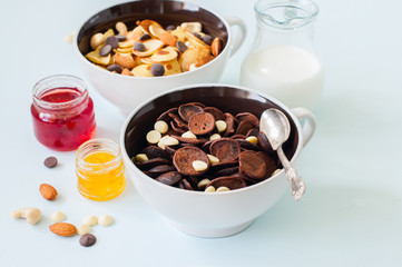 Chocolate and vanilla tiny pancake cereals with nuts and chocolate drops in a bowls.