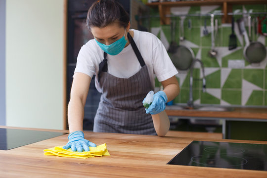 Woman in protective mask and gloves cleaning kitchen