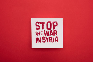 Top view of white placard with stop war in Syria lettering on red background