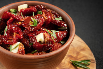 Sun-dried tomatoes with garlic, rosemary and spices in a clay bowl on an olive wood cutting board