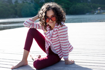 Pretty girl dressed red jeans , sunglasses and white t-shirt relax in the nature alone against the beautiful view of mountain, forest, sunrise and lake.