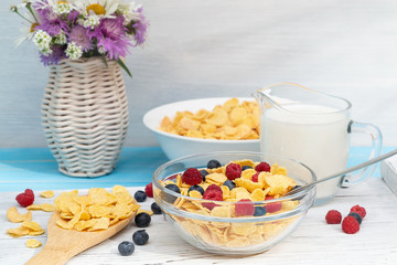 Healthy summer breakfast - cereal with milk and fresh berries in bowl on table. Light wooden background, wildflowers in vase. Healthy eating concept