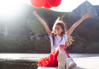 Pretty girl dressed red skirt ans white t-shirt relax in the nature with fun against the beautiful view of mountain, forest and lake, Preteen kid holding balloons