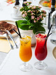 Two cold lemonades berry and passion fruit . Drink with ice. The glasses are on a white tablecloth. Desserts and flowers are in the background. Menu for bars, cafes and restaurants. Vegetarian.