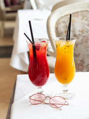 Two cold lemonades berry and passion fruit . Drink with ice. The glasses are on a white tablecloth. Rose-colored glasses lie next to it. Menu for bars, cafes and restaurants. Vegetarian.