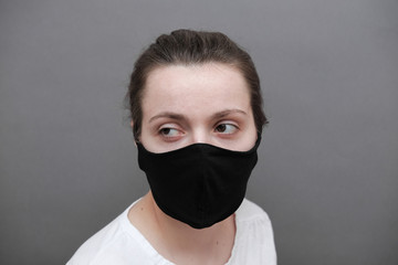 A woman in a black protective medical mask looks at the camera with tired eyes.
