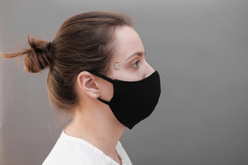 Chipization of people. A microchip implanted on a person's temple during a coronavirus disease to monitor life indicators. A woman in a black protective medical mask.