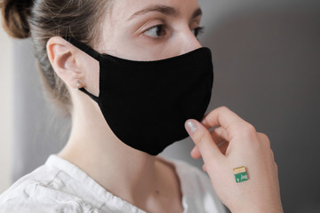 A microchip implanted on a person's hand during a coronavirus disease. A woman in a black protective medical mask.