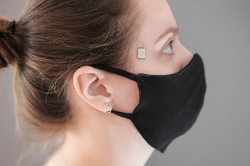 Chipization of people. A microchip implanted on a person's temple during a coronavirus disease to monitor life indicators. A woman in a black protective medical mask.