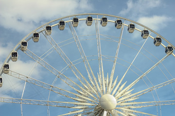 Looking up at a giant ferris wheel backed by a blue and cloud filled sky