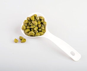 capers in a white spoon, isolated on a white background