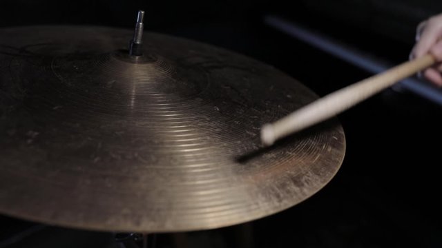 Playing hi-hat musical instrument. Hands of musician drummer holding drum sticks hitting on crash cymbal on dark background, closeup view. Drum cymbal vibration