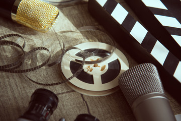 Film reel, movie clapperboard, two microphones and an old movie camera with two lenses on a table with a gray