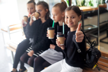 Close-up of girl hand finger up against the group of female preteen kids  communicate together outdoor and drinking warm coffee drink in takeaway paper glasses