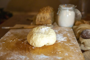 Kneaded dough for pastry laying on wooden board. Fresh cereal loaf flour in glass jar. Selective focus. Studio shot. Side view. Homemade bakery and cooking at home concept