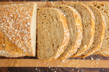 Whole grain French loaf cut in slices on chopping board. Closeup shot, top view. Traditional bread or baker job concept