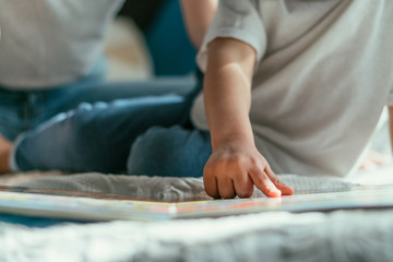 cropped view of toddler boy pointing with finger at book near mother in bedroom