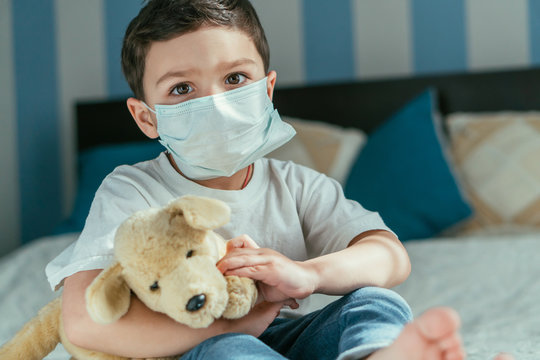 selective focus of toddler boy in medical mask holding soft toy at home