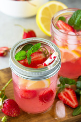Summer drink refreshing close-up. Lemonade with fresh strawberries, ice and lemons on a light stone countertop.