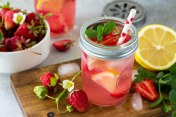Summer drink refreshing. Lemonade with fresh strawberries, ice and lemons on a light stone countertop.
