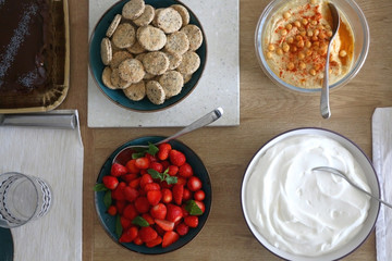 Brunch food served on a table: hummus, salty crackers, strawberries and whipped cream. Top view.