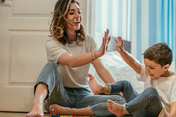 happy mother giving high five to toddler son while sitting on floor