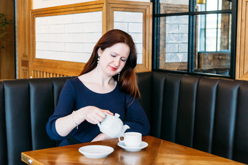 A girl of European appearance in a cafe, drinking tea or coffee from a mug, conversation, meeting, lunch, waiting for a friend