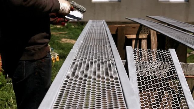 Fence constructing works. Painting metal fence parts using pain brush. Worker hand with tool closeup. Brush applies grey (gray) paint to steel expanded (plain) sheet and rolled metal rectangular pipes