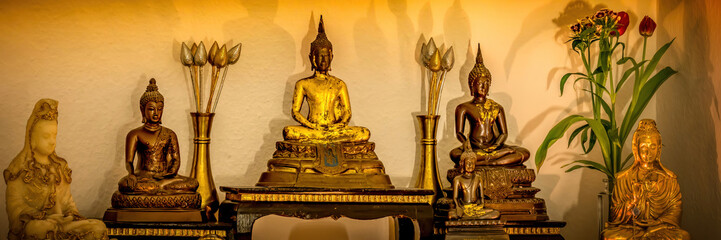 Buddhas on a cupboard in a living room with some candles for praying at home in HDR as a panorama.