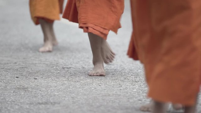 Low section of Buddhist monks wearing saffron robes while walking barefoot on street in city - Luang Prabang, Laos