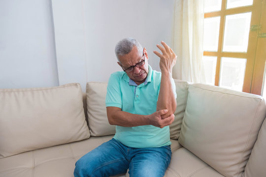 Older Man With Arm Pain Sitting On His Couch At Home, Feels Sick