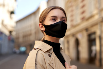 Fototapeta premium Woman wearing trendy fashion outfit during quarantine of coronavirus outbreak. Model dressed protective stylish handmade face mask. Tourist walkin on empty street. Beautiful blonde woman with fashion 