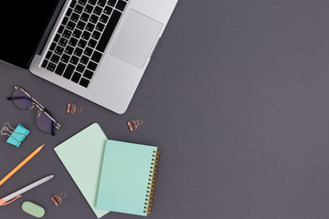 Top view of laptop, glasses and stationery on a dark gray background. Student workspace concept...