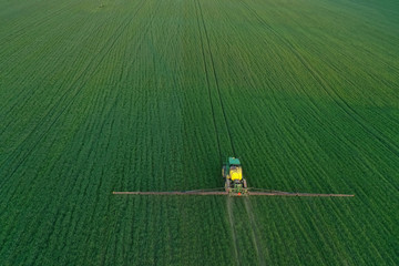 In the spring season, the farmer sprays wheat or barley with insecticides and fungi with a tractor. Top view, aerial view of the mounted tractor while working. Pest County / Hungary - 05.05.2020.