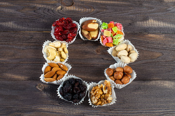 A serving of assorted candied fruit, dried cherries, almonds, raisins, walnuts and hazelnuts in paper muffin cups on a dark wood background. In the shape of a ring.