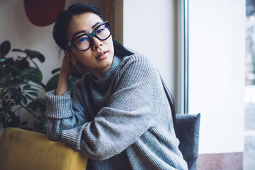 Relaxed ethnic woman sitting on windowsill in living room