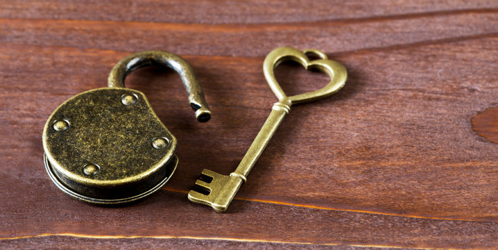 Gold vintage heart key and unlocked padlock on wooden background. Sweet home concept, web banner.
