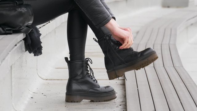 Close up shot of stylish woman tying up her black boots outside, she's addicted to black color