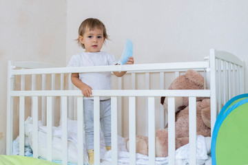 quarantine coronavirus covid-19 pandemic concept. a little cute baby is in a crib at home in safety, looking seriously at the camera and holding a medical mask. copy space