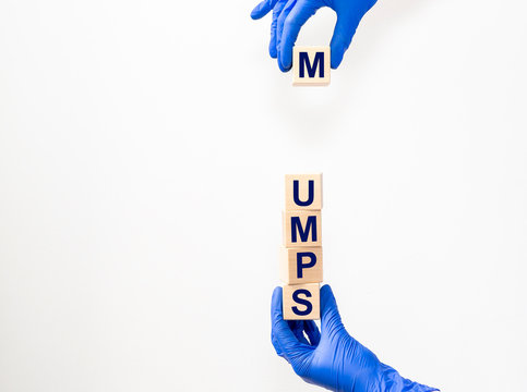 Mumps word on cube blocks in hands in protective gloves isolated on a white background. Copy space. Medical concept