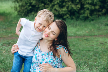 a young mother with a young son sit on the grass in the park. Family holidays in nature. A young son hugs his mother. Pregnant girl with a child walking in the garden.