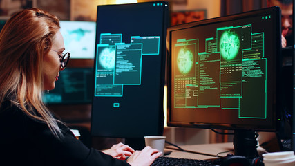 Girl hacker looking at super computer with multiple monitors while writing a malware.