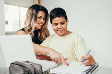 Young student doing homework at home with laptop helped by his mother. Mom teaching his son. Education, family lifestyle, homeschooling concept