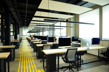 Young people working at laptops at the large computer room, office