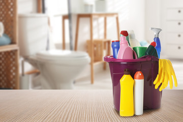 Bucket with cleaning supplies on wooden table in bathroom, space for text